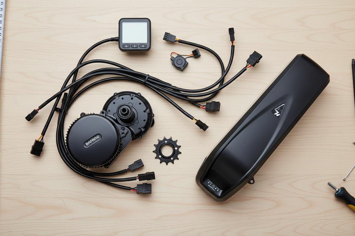 Kit de conversion vélo électrique Bafang BBS02 avec moteur, écran et câbles disposés soigneusement sur un établi en bois clair