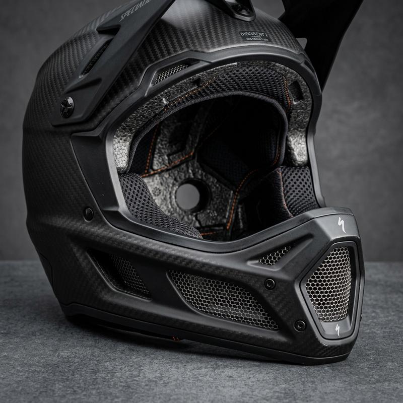 Gros plan macro d'un casque de VTT intégral haut de gamme montrant la structure en fibre de carbone et les détails des aérations de la mentonnière.